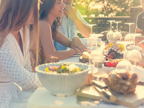 Ihr Portal für Informationen und Services rund um Ihre Allergiebehandlung Eine Gruppe von Menschen sitzt an einem Picknicktisch im Freien und genießt eine Mahlzeit. Der Tisch ist mit Salat, Obst und Brot gedeckt, umgeben von Gläsern und Tellern. Die untergehende Sonne wirft einen warmen Schein über die Szene und schafft eine entspannte Atmosphäre.